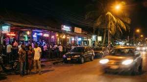 夜晚街道，霓虹酒吧、棕櫚樹和行駛中的汽車在路燈下