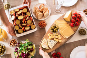 People serving a wooden board of cheese bread salad and roasted veggies at a table. — MacBook Air M2 壁紙