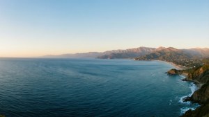 海岸場景，藍色海洋、沙灘、懸崖和山脈在晴朗的天空下