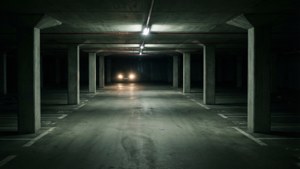 一輛汽車在黑暗空蕩的混凝土停車場中亮著車頭燈駛近