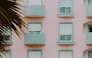 粉紅色公寓大樓，前景有青綠色陽台和棕櫚葉。