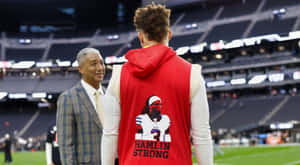 穿著「HAMLIN STRONG」背心的足球員在球場上與穿西裝的男子交談。