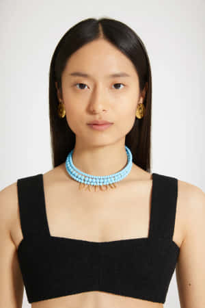 身穿黑色上衣的女士佩戴綠松石珠頸鏈和金色耳環。