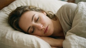 一個女人在床上睡得很沉，床上有白色枕頭和米色亞麻床單。