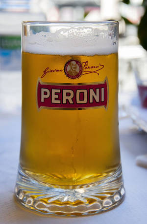 一個Peroni啤酒杯，裝有金黃色液體和白色泡沫，放在戶外桌子上。
