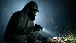 穿著防護服的人士在夜間用手電筒檢查泥中的物體。