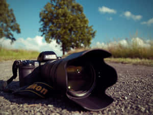 一部 Nikon DSLR 相機躺在碎石上，背景有樹木和藍天。