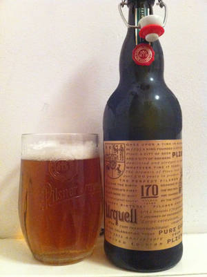 一瓶Pilsner Urquell啤酒旁邊放著一杯裝滿琥珀色啤酒和泡沫的玻璃杯。