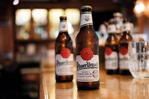 Pilsner Urquell 啤酒瓶在酒吧中，帶有溫暖燈光和模糊背景。
