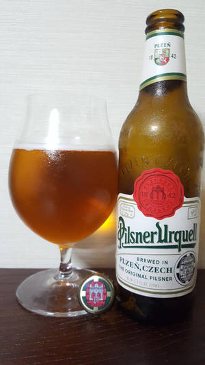 木桌上的一瓶Pilsner Urquell啤酒和一個玻璃杯。