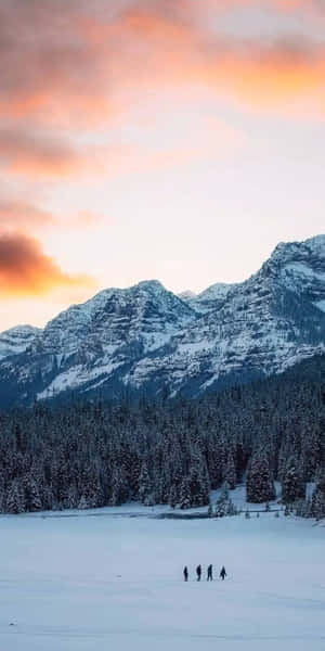 日落時分，四個人在雪山附近嘅冰凍湖泊上行走。 — 冬日美學 壁紙