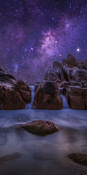 瀑布在紫色星空下在岩石之間流動。