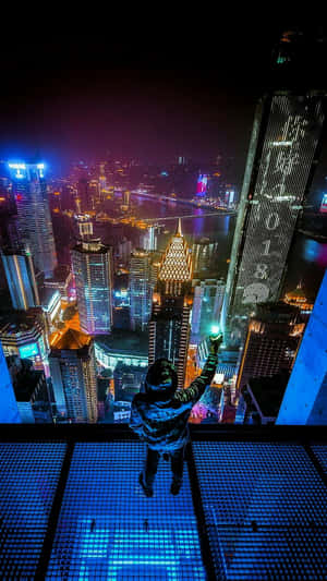 夜晚喺玻璃露台上俯瞰發光城市嘅人