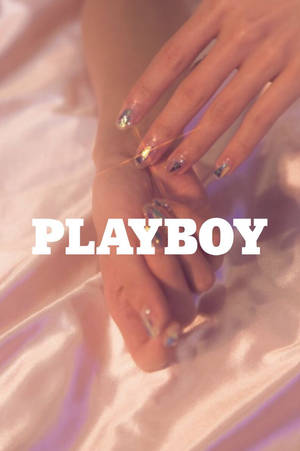 帶有閃亮指甲的手放在緞面布料上，帶有Playboy標誌。