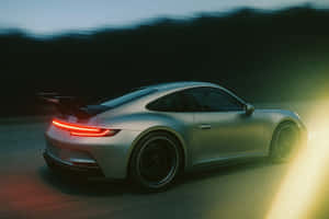 銀色保時捷911 GT3 RS在黃昏時分疾馳，紅色尾燈發光，帶有動態模糊