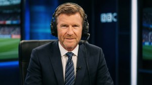 身穿西裝和耳機的BBC體育評述員在廣播攝影棚內微笑。