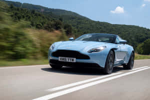 淺藍色Aston Martin在風景優美的山路上疾馳。 — MacBook Pro M2 壁紙