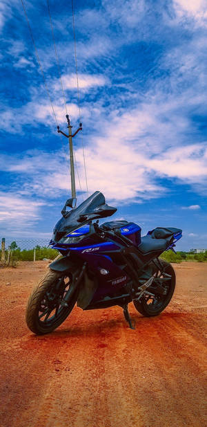 藍色Yamaha R15電單車停在泥路上，背景是晴朗的藍天和白雲。