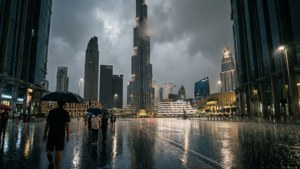 人們撐著雨傘在雨中走在濕漉漉的城市廣場上，背景是高樓大廈。