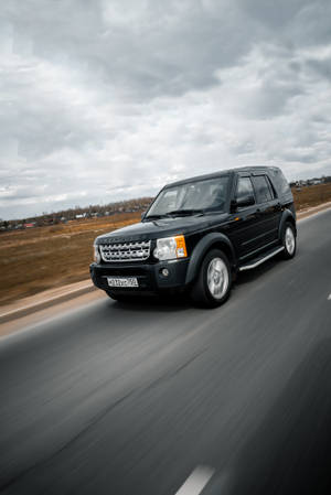 黑色 Land Rover SUV 在陰天下的鄉村道路上疾馳。