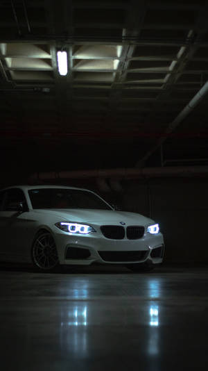 白色BMW汽車，車頭燈明亮，停泊在黑暗的地下停車場，地板濕滑有倒影。