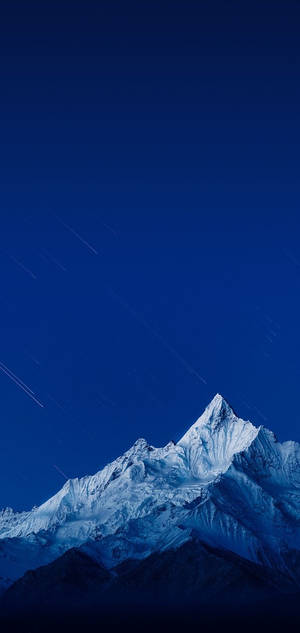 在繁星點點的夜空下，帶有可見星軌的雪覆蓋山頂。 — Realme 壁紙