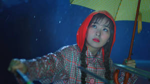 夜晚雨中，穿著紅色連帽雨衣的女子撐著黃色雨傘。