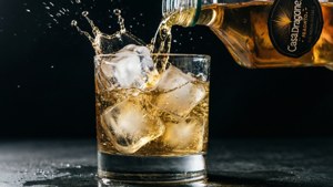 金色龍舌蘭酒倒在冰塊上，玻璃杯中產生戲劇性的水花。