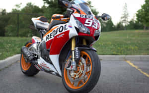 紅色、白色和橙色的Repsol Honda賽車電單車停在瀝青路上，靠近草地。