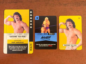 三張 Rick Rude 的 WWE 收藏卡放在木桌上。 — 摔角 GIF 壁紙