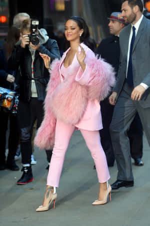 Rihanna 穿著粉紅色毛皮大衣和高跟鞋走在城市街道上。 — Vivo Pad 壁紙