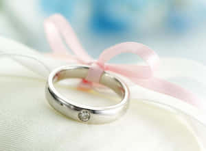 銀色結婚戒指，鑽石和粉紅色絲帶在白色布料上。