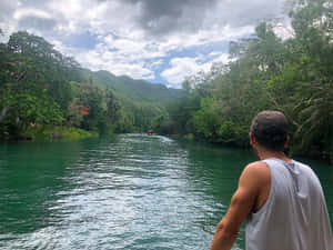 戴帽子的男子在叢林河流的船上，有山和陰天