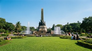 人們在陽光明媚的公園裡，在噴泉和紀念碑附近的草地上放鬆
