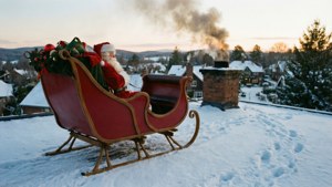 聖誕老人坐在紅色雪橇上，在積雪屋頂俯瞰村莊，煙囪冒煙