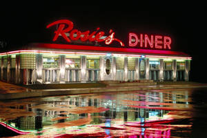 Rosie's Diner 被霓虹燈照亮，倒映在夜間濕漉漉的路面上。