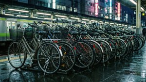 單車停泊在雨中的火車站夜晚，霓虹燈光反射在濕漉漉的路面上。