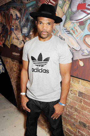 戴黑色軟呢帽、身穿灰色adidas T恤的男人站在貼有運動鞋海報的磚牆附近。 — 肖像 壁紙