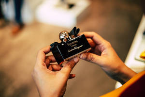 雙手拿著 Salvatore Ferragamo 的黑色和金色香水瓶。
