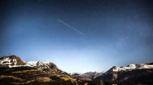 繁星點點的夜空下，白雪覆蓋的山脈，伴隨著一道飛機尾跡。 — 自然 壁紙