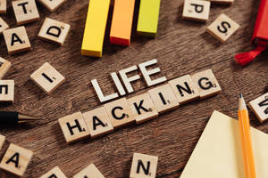 Scrabble 字母磚在木桌上拼出 life hacking，旁邊有彩色積木和鉛筆。