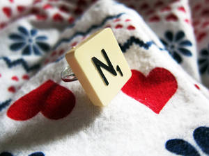 一個帶有字母 N 的 Scrabble 字母牌，放在心形圖案的布料上。