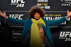 UFC活動中留爆炸頭戴太陽眼鏡的男人，身穿藍綠色外套和黃色圍巾。