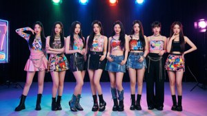 七位K-pop偶像穿著鮮豔服裝，在彩色聚光燈照亮的舞台上擺姿勢。