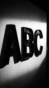 黑色ABC字母安裝在白色牆壁上，帶有定向照明產生的強烈陰影。
