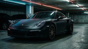 啞光黑色保時捷911 Turbo停放在霓虹燈照亮的地下停車場，帶有反光表面。