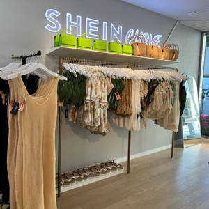 SHEIN CURVE商店內部，有連身裙同涼鞋嘅貨架，喺霓虹燈牌下面。