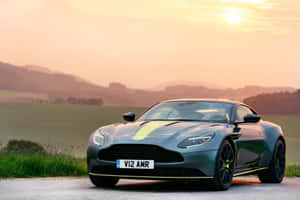 時尚灰色 Aston Martin DB11 AMR 帶有螢光綠色點綴，停泊在金色日落下的鄉村道路上。 — Surface Pro 壁紙