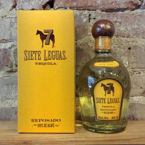 Siete Leguas龍舌蘭酒瓶和盒子放在木質表面上，背景是磚牆。