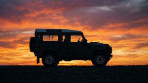 在荒蕪的景觀上，日落時分 Land Rover Defender 的剪影。